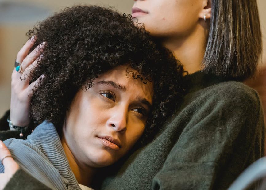 serious young woman embracing sad black girlfriend